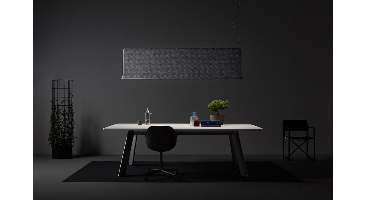 large grey acoustic light suspended from ceiling in dark room above table